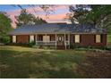 Inviting brick home featuring a cozy front porch, manicured lawn, and mature trees under a picturesque evening sky at 2301 Sharon Se Ct, Conyers, GA 30013