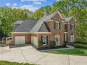 View of a two-story brick home with a three-car garage and a spacious concrete driveway at 4750 Spring Wood Trce, Cumming, GA 30041