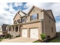 A low angle view of a two-story brick home with a front porch and attached two-car garage in a suburban neighborhood at 570 Eldridge Dr, Suwanee, GA 30024