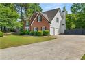 View of the home showing the two-car garage, well manicured lawn, and mature trees at 990 Lilac Arbor Rd, Dacula, GA 30019