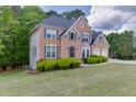 View of a brick house on a green lot with trimmed shrubs, side yard, and a two-car garage at 4290 Grand Teton Pkwy, Suwanee, GA 30024