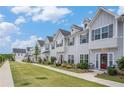 Row of new townhomes with gray siding, red doors, green lawns, and sidewalks under a blue sky at 1702 Prospect Way, Conyers, GA 30094