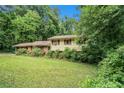 View of single Gathering home surrounded by mature trees and an overgrown front yard at 2214 River Rd, Ellenwood, GA 30294
