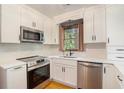 Modern kitchen with stainless steel appliances, white cabinets, stone backsplash, and a view of the trees at 929 Hampton Nw Trl, Lilburn, GA 30047