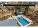 An aerial view of a virtually staged backyard pool with modern design and a pool house surrounded by trees and landscaping at 6265 Reives Rd, Cumming, GA 30041