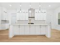 Bright kitchen with a large island, white cabinets, a stainless-steel range hood, and modern lighting fixtures at 225 Alcovy Cir, Covington, GA 30014