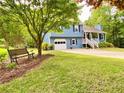 Landscaped front yard with a blue home, bench, and mature trees providing shade at 5364 Muirwood Pl, Powder Springs, GA 30127