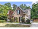 An eye-level shot of a well-manicured brick home with green lawn and trees, showcasing its exterior charm at 1235 Legend Run, Alpharetta, GA 30005