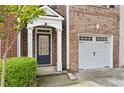 Welcoming brick townhouse entry featuring classic architectural details, a garage, and manicured bushes at 1880 Garbrooke Cv, Lawrenceville, GA 30046