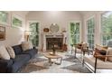 Cozy living room with a fireplace, light hardwood floors, modern furniture, and three large windows providing natural light at 310 Tradea Tarn, Roswell, GA 30076