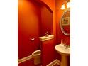 Stylish powder room with an oval mirror, pedestal sink, and vibrant orange walls at 7550 Star Magnolia, Lithonia, GA 30058