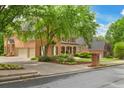 Charming brick home showcasing a three-car garage, manicured lawn, and inviting covered front porch at 120 Burford Holw, Alpharetta, GA 30022
