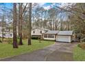 View of the home's front, long driveway, lawn, and mature trees providing shade at 2325 Lago Dr, Jonesboro, GA 30236