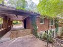 View of brick exterior with covered patio, stone foundation, and overgrown foliage at 668 Lynn Sw Cir, Atlanta, GA 30311