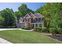 Charming two-story brick home with an attached two-car garage surrounded by mature trees and green lawn at 7014 E Hills Way, Woodstock, GA 30189