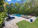 Backyard featuring a luxurious pool and hot tub combo, surrounded by a paved patio and lush greenery at 2325 Manor Creek Ct, Cumming, GA 30041