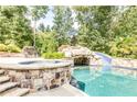 Backyard pool featuring a stone grotto with slide, surrounded by lush greenery and a stone patio with seating at 4090 Cooks Farm Nw Dr, Kennesaw, GA 30152