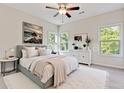 Bright bedroom featuring a ceiling fan, large bed, white dresser and windows overlooking the lush green yard at 70 Wheeler Lake Path, Dallas, GA 30157