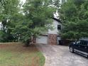Home exterior with attached garage, driveway, brick accents, siding, and surrounding trees at 135 Golden Hills Dr, Woodstock, GA 30189