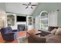 Cozy living room with a fireplace, built-in shelving, a ceiling fan, and a large window at 3820 Pheasant Run Trce, Cumming, GA 30028
