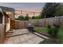 Cozy backyard patio area features stone pavers, wooden fence, string lights, and a grill at 3872 Francis Dr, Powder Springs, GA 30127