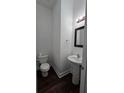 Half bathroom featuring a pedestal sink, toilet, modern mirror, and dark wood-like flooring at 2275 Copper Trail Ln, Buford, GA 30519