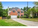 Two-story brick home with a spacious driveway, attached garage, complemented by lush greenery and mature trees at 7035 Hampton Bluff Way, Roswell, GA 30075