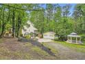Landscaped yard featuring a charming home, detached garage, and gazebo surrounded by lush greenery at 510 Aiken Dr, Dallas, GA 30157
