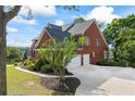View of the side of the brick home, featuring an attached two-car garage and a wide driveway at 5260 Harbury Ln, Suwanee, GA 30024
