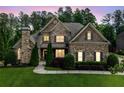 Evening view of brick home boasting manicured landscape, stone chimney, and inviting illuminated windows at 390 Scott Farm Dr, Powder Springs, GA 30127