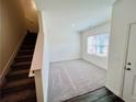 Bright living room features plush carpeting, staircase access, and a large window for natural light at 7775 Sudbury Cir, Covington, GA 30014