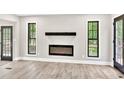 Modern living room features a sleek fireplace, wood-look floors, and black framed windows with natural light at 7619 Campground Rd, Cumming, GA 30040