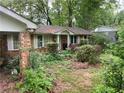 View of the home's side and front shows a red brick exterior and an overgrown front yard at 1481 Pine St, Stone Mountain, GA 30087