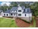White two-story home with a manicured lawn, black shutters, brick foundation, and mature trees at 7620 Breeze Bay Rd, Cumming, GA 30041