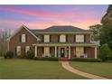 Charming brick home with a covered porch, well-manicured lawn, and inviting curb appeal at dusk at 210 Little River Farms Trl, Canton, GA 30115