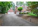 Large, brick home featuring a three-car garage and a long driveway, surrounded by lush landscaping and mature trees at 6450 Oak Valley Dr, Cumming, GA 30040
