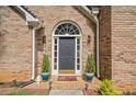 Close up of arched entryway with slate gray door, brick facade, and potted greenery at 8035 Canter Ln, Alpharetta, GA 30009