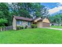 View of the front of the house with a green lawn and mature trees and shrubs in the background at 8350 Gledstone Way, Fairburn, GA 30213