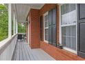 Covered porch with gray wood floor, brick walls, black shutters on windows, and seating area at the end at 2530 River Run Dr, Dacula, GA 30019