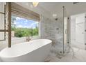 Bright bathroom featuring a freestanding tub, glass-enclosed shower, and large window with backyard views at 7059 Hunters Rdg, Woodstock, GA 30189