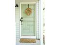 Inviting mint green front door adorned with a decorative wreath, set against light gray siding and a woven doormat at 5419 S Lake Dr, Douglasville, GA 30135