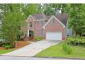 Classic brick home with arched window, lush landscaping, and a wide driveway leading to a two-car garage at 7435 Woodruff Way, Stone Mountain, GA 30087