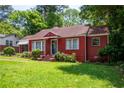 Red brick house with a green lawn, featuring mature trees and decorative front door at 3020 Washington Rd, East Point, GA 30344