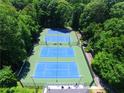 Aerial view of three well-maintained blue tennis courts surrounded by lush green trees at 2628 Amberly Dr, Dunwoody, GA 30360