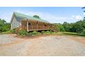 Inviting home featuring a green roof, long porch, landscaped yard, and spacious gravel driveway at 220 Mountain Creek Rd, Bowdon, GA 30108