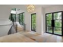 Bright foyer features staircase, hardwood floors, modern light fixture, and black frame windows with wooded views at 130 Nova Ln, Roswell, GA 30075