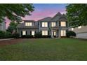 Charming two-story home with a well-kept lawn, surrounded by lush trees and illuminated by the setting sun at 4218 Sandy Branch Dr, Buford, GA 30519
