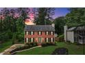 Charming two-story brick home boasts lush landscaping, a well-manicured lawn, and classic black shutters at dusk at 225 Carriage Station Cir, Roswell, GA 30075