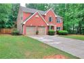 Charming two-story red brick home featuring a well-manicured lawn, attached two-car garage, and lush landscaping at 5765 Woodstone Dr, Cumming, GA 30028