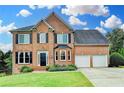 Traditional two-story brick home featuring a manicured lawn, flower beds and a two-car garage, set against a blue sky at 3760 Ansley Park Dr, Suwanee, GA 30024